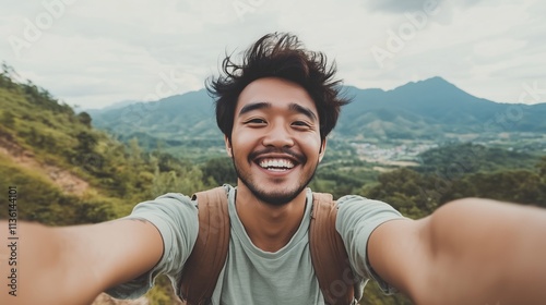 In a picturesque valley surrounded by majestic mountains, a young Asian man poses happily for a selfie, enjoying the stunning natural beauty of the landscape.