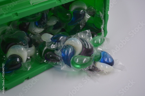 Things, objects for daily use, cleansing. Round polyethylene capsules filled with white, blue, green, purple laundry detergent, clothes located in a green plastic container on white plastic backgroud. photo