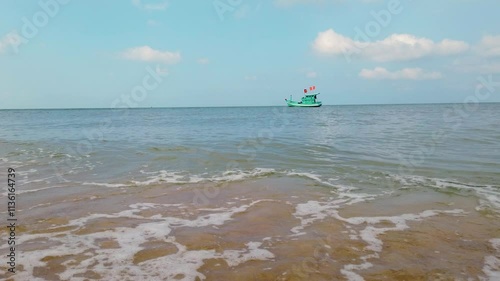 A green fishing boat with Vietnamese flags bobs on the waves anchored on a sunny day