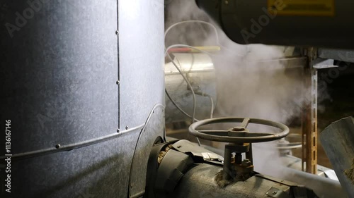 Steam escaping from a large industrial pipe with a valve rises and dissipates, showcasing the interplay of heat and pressure in manufacturing environments. Heavy industry concept. Chemical and
