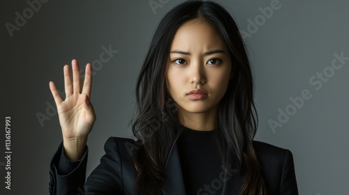 Woman in Black Blazer Holding Hand Up Against Gray Background