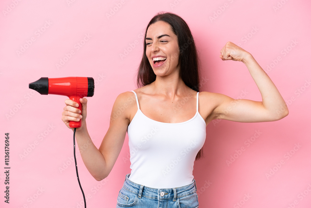 Young caucasian woman holding a hairdryer isolated on pink background celebrating a victory Young caucasian woman holding a hairdryer isolated on pink background celebrating a victory