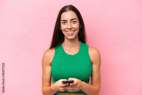 Young caucasian woman isolated on pink background sending a message with the mobile