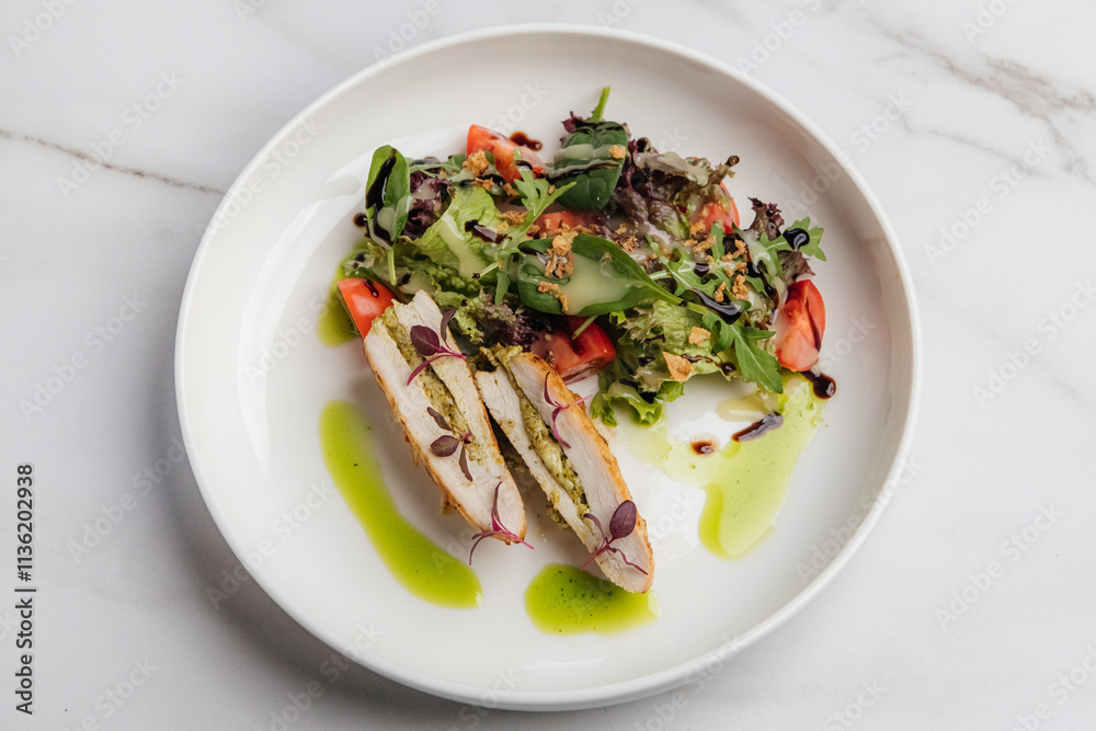Slices of grilled chicken breast stuffed with pesto, paired with a fresh salad of tomatoes and arugula, elegantly arranged on a white plate. Restaurant or cafe menu, cookbook recipe Slices of grilled chicken breast stuffed with pesto, paired with a fresh salad of tomatoes and arugula, elegantly arranged on a white plate. Restaurant or cafe menu, cookbook recipe