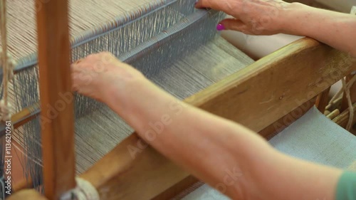 women's hands on an ancient wooden loom weaves linen fabric