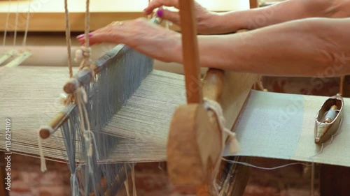 women's hands on an ancient wooden loom weaves linen fabric
