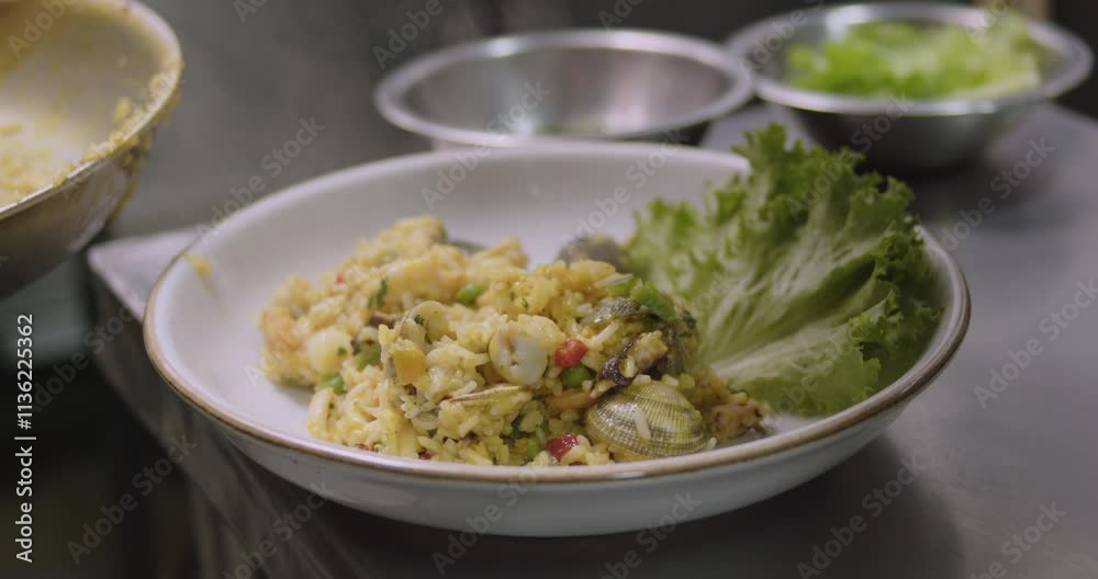 putting the Peruvian seafood rice in white plate with fresh lettuce, on a restaurant kitchen's table putting the Peruvian seafood rice in white plate with fresh lettuce, on a restaurant kitchen's table