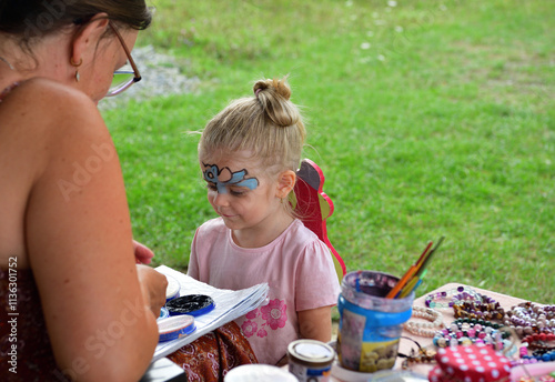 An artist painter paints a picture on the face of a little girl