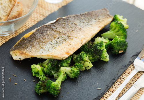 Fried fillet of sea bass with garnish of broccoli on black warm stone plate photo