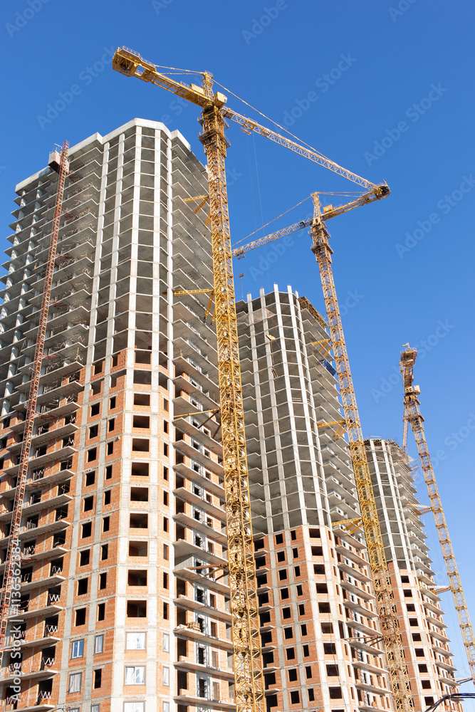 Three new high-rise panel building under construction and tower cranes at work against the blue sky, vertical photo. Three new high-rise panel building under construction and tower cranes at work against the blue sky, vertical photo.