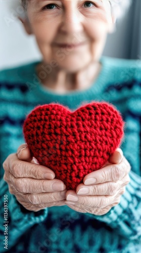 Elderly woman expresses love and care by holding a red knitted heart in a warm, gentle setting