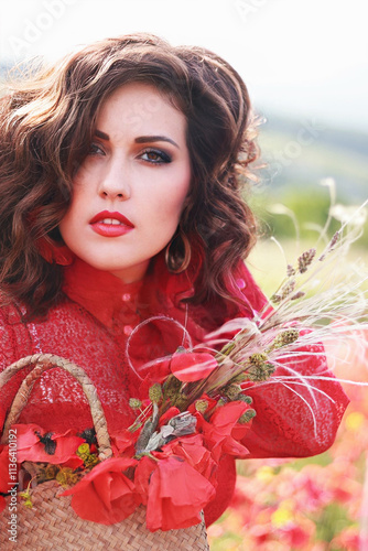 A girl in a red dress and hat stands in a field of poppy flowers at sunset
