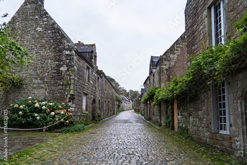 Les ruelles pavées de Locronan après la pluie, les maisons en pierre semblent endormies sous un ciel couvert, et les pavés mouillés reflètent la lumière tamisée.