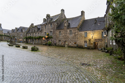 Une place pittoresque de Locronan, entourée de maisons en pierre typiques. Le ciel gris d'automne et les pavés mouillés créent une ambiance tranquille et chaleureuse. photo