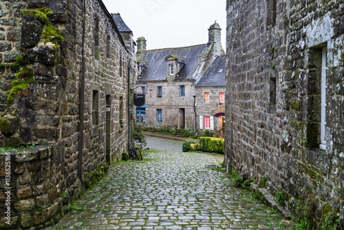 Fototapeta Naklejka Na Ścianę i Meble -  Une rue de Locronan bordée de maisons anciennes aux toits en ardoise, le ciel gris d'automne se reflète sur les pavés mouillés.