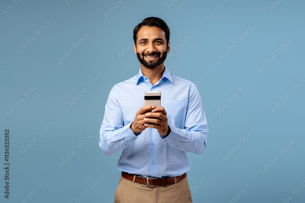 Fototapeta premium Portrait of smiling, happy bearded middle aged Indian man holding mobile phone, using mobile app