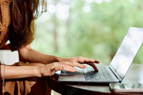 Young woman in brown dress working on laptop outdoors, expressing concentration and focus, with natural greenery in the background, ideal for remote work themes