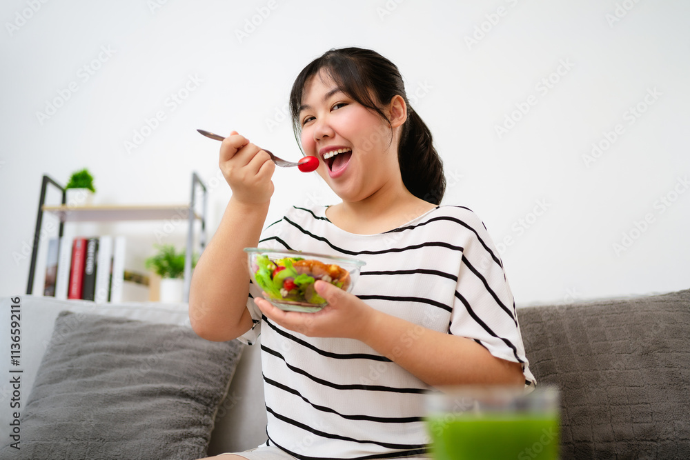 Beautiful Asian woman eating salad, holding a glass bowl and using a fork to pick up a tomato to eat Beautiful Asian woman eating salad, holding a glass bowl and using a fork to pick up a tomato to eat