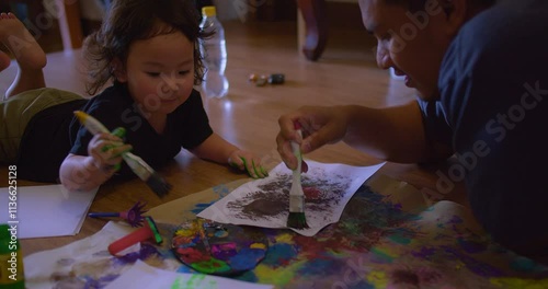 A Asian father and young daughter child engage in creative painting on the floor in cozy home, fostering imagination and bonding in a warm home setting.
