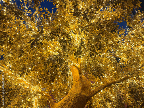 Golden tree leaves with LED twinkle lights or icicle lights. Big gold tree decorated with yellow lights to celebrate seasons greetings, holiday season of Christmas and new year. Night shot. photo