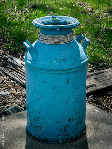 Decorative Milk Can. An aqua blue painted vintage metal milk can at the edge of a patio  backlit by the afternoon sun.