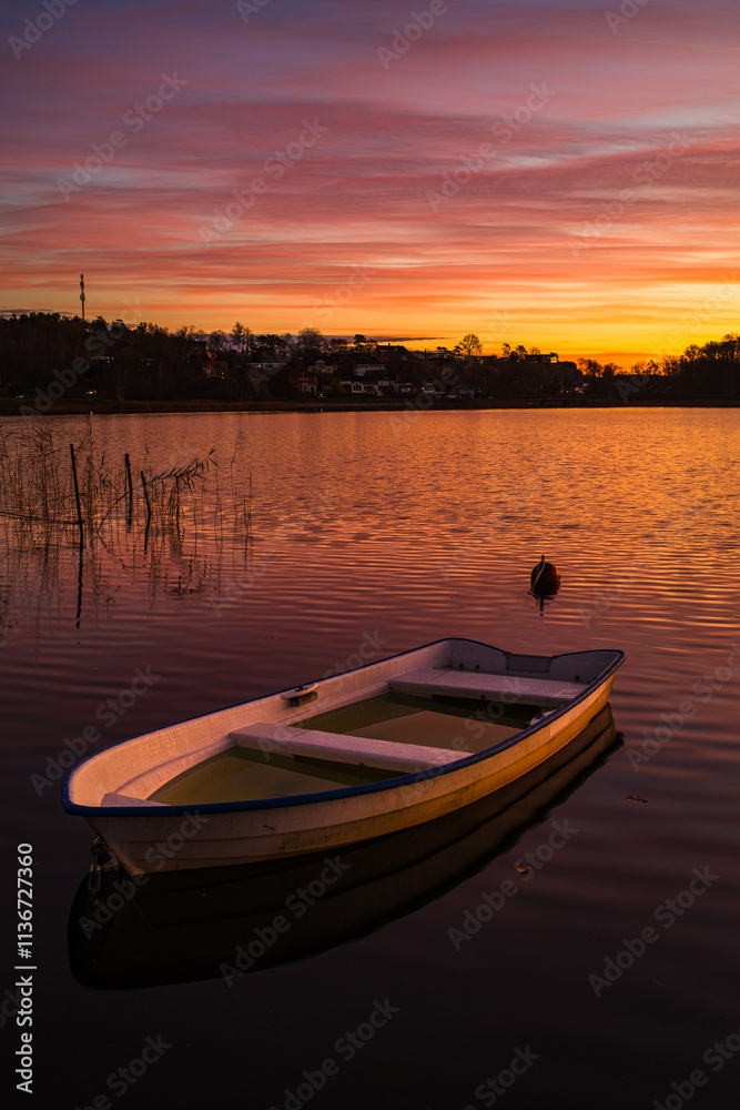 Sunset over calm water with a small boat anchored at lakeside resort location Sunset over calm water with a small boat anchored at lakeside resort location
