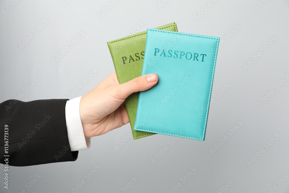 Woman holding passports in bright covers on grey background, closeup Woman holding passports in bright covers on grey background, closeup