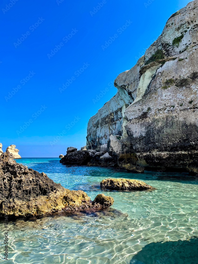 Fototapeta premium Rock cliff with turquoise quiet waters in a blue Mediterraneam Beach in Puglia, Italy