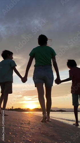 Family holding hands walking on a beach at sunset. Warm light and reflections on the wet sand. Concept: family love and togetherness.