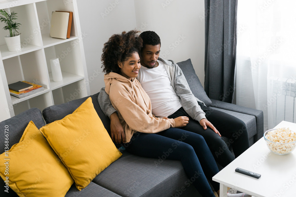 African American couple wife husband watching movie. Family pastime and leisure, watch television, rest. Relaxed man and woman watching TV series together sitting on couch at home enjoying eating