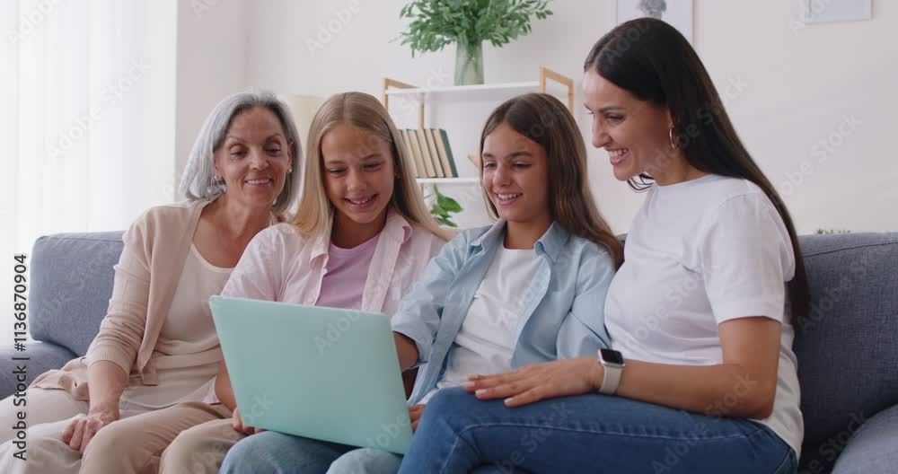 Happy family of grandmother, mother and kids sitting on sofa at home using laptop together, watching movie or news in social media. Generations and technology concept. 4k video. Slow motion video.