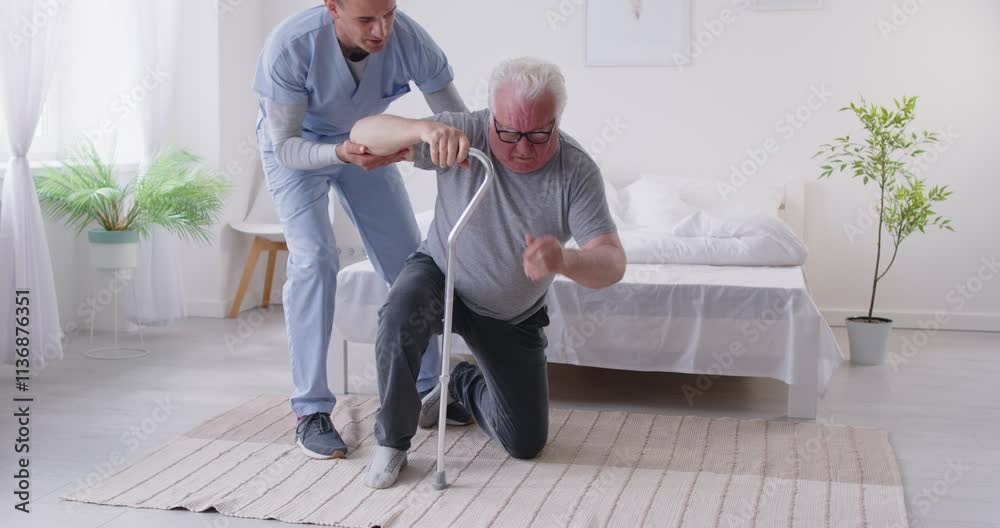 Caring young male caregiver running over to help elderly man to get up after falling in rehabilitation clinic. Friendly nurse providing assistance to pensioner patient, supporting him during walking.
