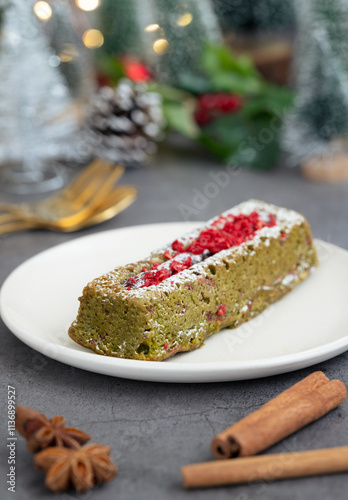 A matcha green tea cake in a plate topped with zest of red velvet raspberry with star anise and cinnamon stick and Christmas festive ambiance decoration with bokeh light illumination in background.