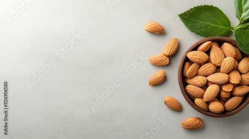 A collection of almonds in a wooden bowl is paired with fresh green leaves on a light gray surface, illustrating a nutritious and aesthetically pleasing composition. photo