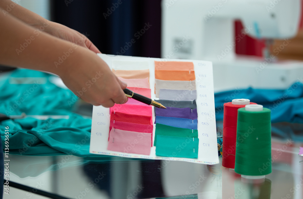 Fototapeta premium A person is holding a pen and looking at a piece of paper with a color chart. The chart has a range of colors, including pink, purple, green, and blue