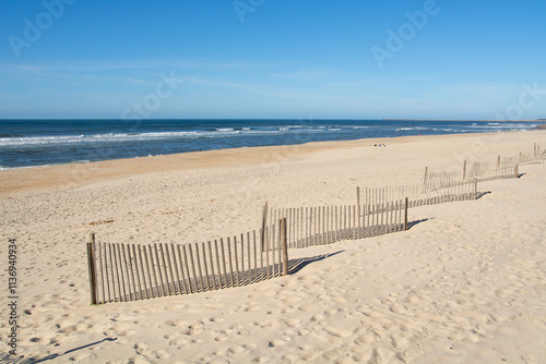 Detail of a light wooden railing made of sticks placed on the white sand of a beach and netx to de sea at Costa Nova in Aveiro, Portugal. photo