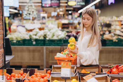 Woman choosing yellow bell peppers in supermarket produce section photo