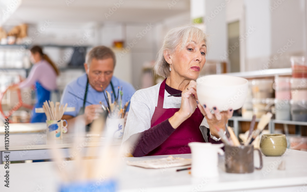 Obraz premium woman covers with white paint almost ready-made jug, which she made herself at pottery workshop