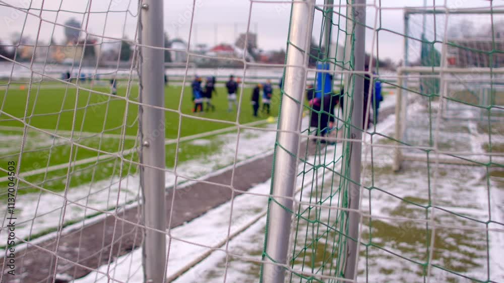 A snowcovered soccer training field with a completely visible goal and players visible in background A snowcovered soccer training field with a completely visible goal and players visible in background