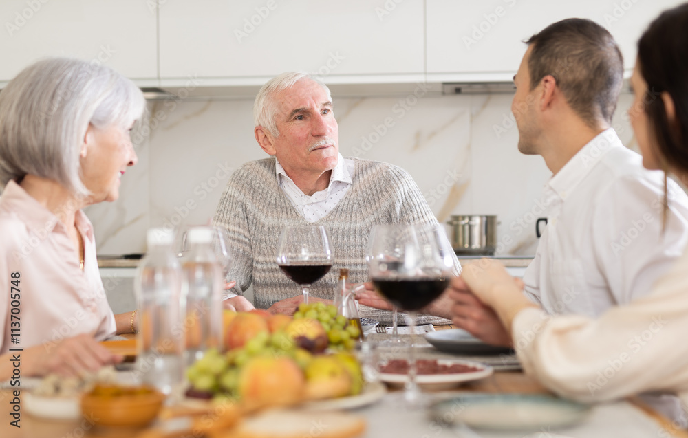 Happy senior man celebrating birthday with wife and adult children over cozy family dinner table served with wine and light snacks.. Happy senior man celebrating birthday with wife and adult children over cozy family dinner table served with wine and light snacks..