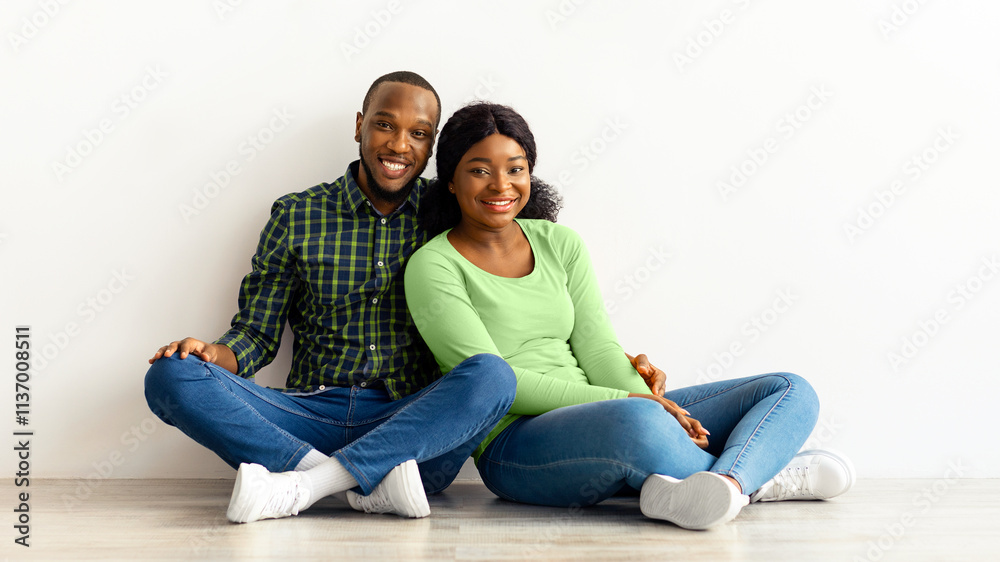Family Housing. Happy Black Couple Sitting Near White Wall With Drawn Roof, Smiling Young Romantic African American Spouses Imagining Their New Home, Planning Relocation, Creative Collage Family Housing. Happy Black Couple Sitting Near White Wall With Drawn Roof, Smiling Young Romantic African American Spouses Imagining Their New Home, Planning Relocation, Creative Collage