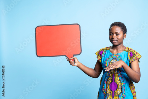 African american woman pointing at red speech bubble in studio, using isolated mockup board to create marketing advertisement. Female model holding cardboard icon sign on camera. photo