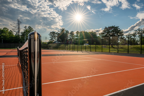 Tennis court net and post on orange and black tennis court - pickleball court with white baseline and black out of bounds	