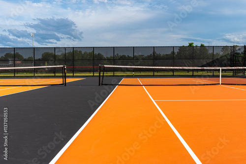 Tennis court net and post on orange and black tennis court - pickleball court with white baseline and black out of bounds	