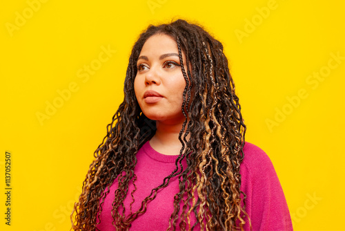 serious plump african american woman with pigtails looking away on yellow isolated background, big plus size girl with dreadlocks photo