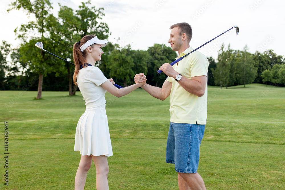 young sporty couple in uniform playing golf on the course and shaking hands, man and woman cheering and competing in golf competition and showing teamwork gesture young sporty couple in uniform playing golf on the course and shaking hands, man and woman cheering and competing in golf competition and showing teamwork gesture
