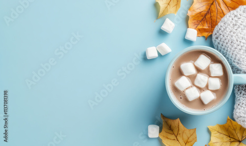 ozy autumn hot chocolate with marshmallows in blue mug surrounded by autumn leaves on soft blue background with copy space photo