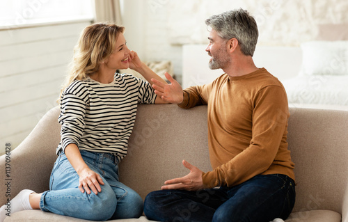 Cheerful Middle Aged Couple Talking And Flirting Enjoying Conversation Spending Time Together Sitting On Sofa At Home. Happy Marriage And Romantic Relationship Concept