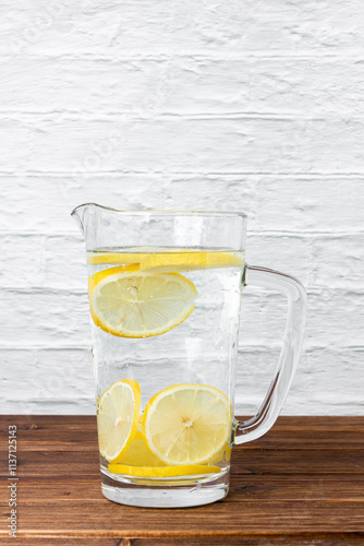 Water with lemons in jug on wooden table.