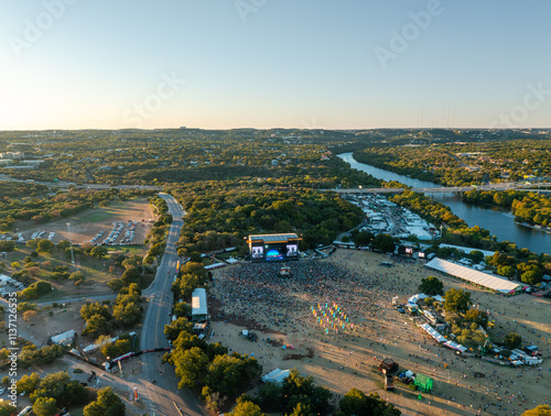 Aerial view of a large crowd gathered for Austin City Limits music festival near Lady Bird Lake during a vibrant sunset